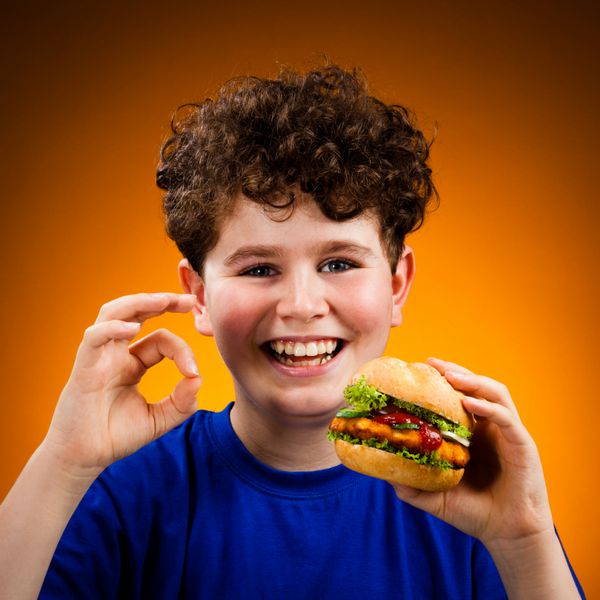 پسر در حال خوردن ساندویچ بزرگ با نشان دادن علامت ok