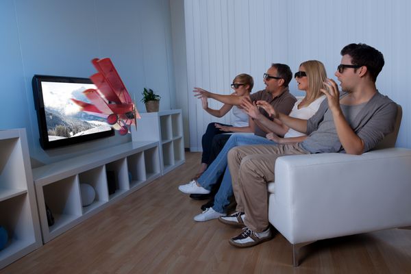تصویر مفهومی خانواده‌ای که در حال تماشای تلویزیون سه بعدی هستند و دستان خود را طوری دراز می‌کنند که انگار می‌خواهند تصویر روی صفحه را لمس کنند