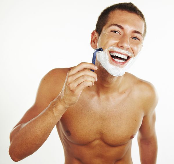 مرد جوان در حال اصلاح در حمام در حالی که به آینه نگاه می کند تیغ را برای ریش رد می کند