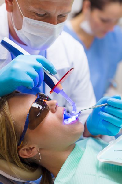 زن جوانی که در کلینیک دندانپزشکی درمان حرفه ای دندانپزشکی انجام می دهد