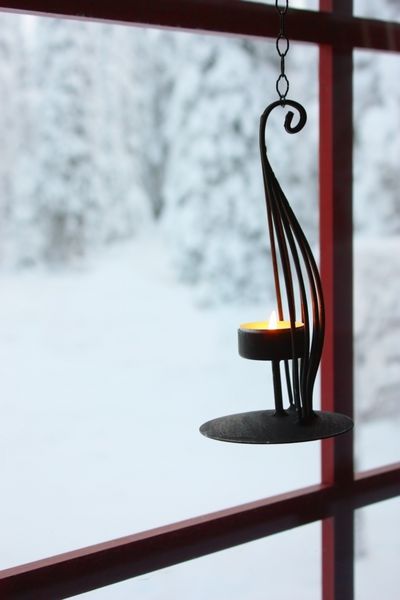 جا شمعی تزئینی با شمع سوزان آویزان روی پنجره به حیاط زمستانی برفی با درختان پوشیده از برف