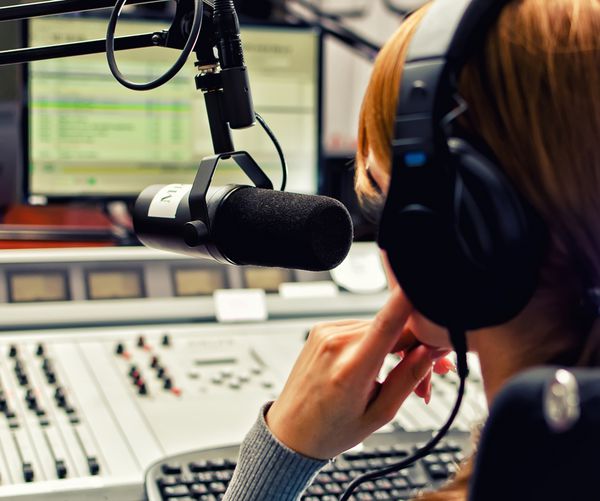 نمای پشت دی جی زن که در مقابل میکروفون در رادیو کار می کند