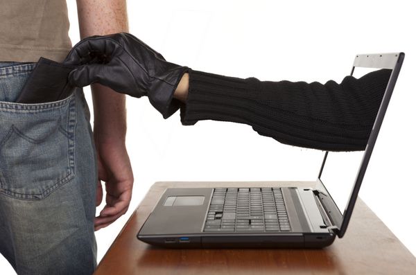 سرقت اینترنتی - یک دست دستکش که از طریق صفحه لپ تاپ برای سرقت کیف پول از مردی دراز می شود