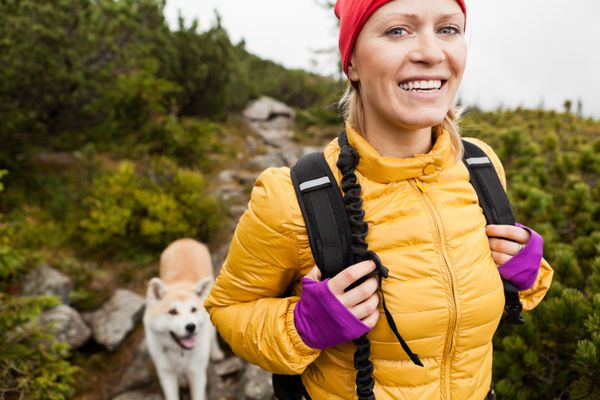 زن خندان شاد در حال پیاده روی در کوه با سگ آکیتا رشته کوه karkonosze زن جوان کوهنورد خندان ورزش و پیاده روی در طبیعت پاییزی