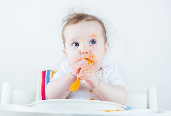 کودک شیرین و آشفته در حال خوردن هویج در صندلی سفید