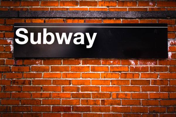 تابلوی ورودی متروی شهر نیویورک روی دیوار آجری