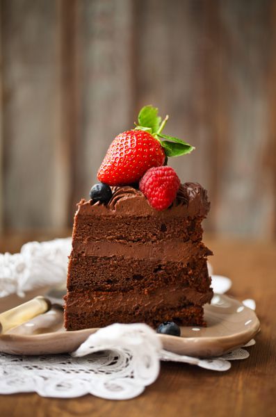 تکه کیک شکلاتی با مایه کیک و توت تازه روی زمینه چوبی