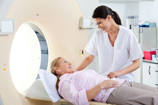 تکنسین رادیولوژی در حال لبخند زدن به بیمار زن بالغ که روی تخت سی تی اسکن دراز کشیده است