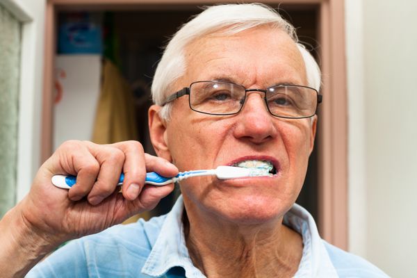 نمای نزدیک مرد سالخورده ای که دندان هایش را مسواک می زند
