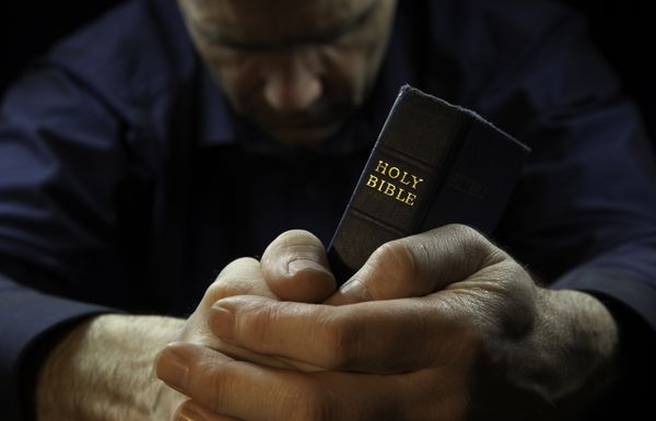 مردی در حال دعا در حالی که کتاب مقدسی در دست دارد