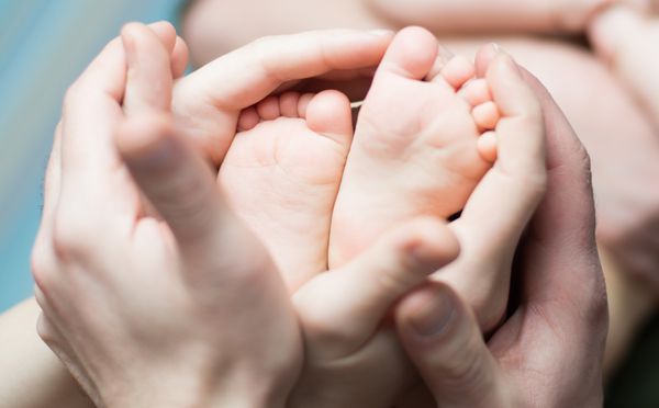 پدر و مادری که با عشق پاهای نوزادان کوچک را در دست گرفته اند