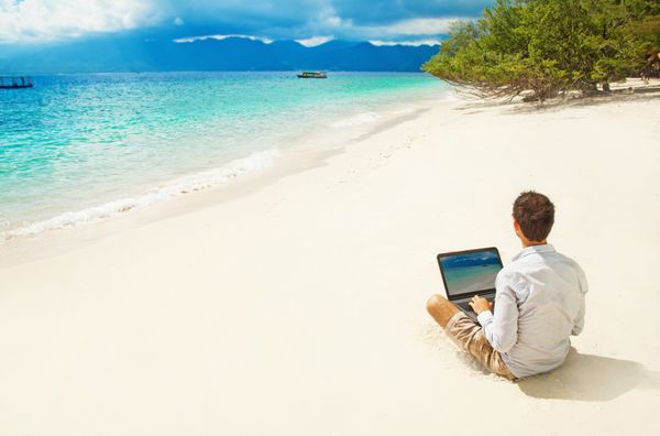 مردی با لپ تاپ در ساحل رنگارنگ جزیره