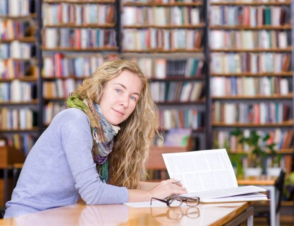 دانش آموز دختر کتاب را در کتابخانه می خواند نگاه کردن به دوربین