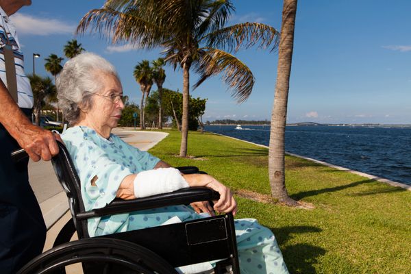 پیرزنی 80 ساله و سالخورده روی صندلی چرخدار در حال نقاهت در فضای باز در محیطی خلیج