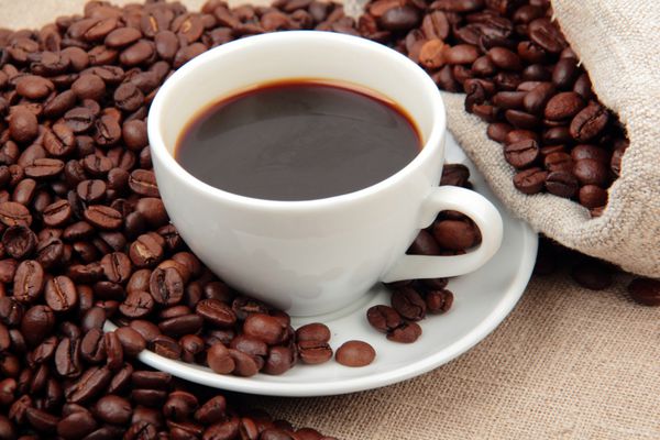 دانه های قهوه برزیلی طبیعی و یک فنجان قهوه روی نوشیدنی