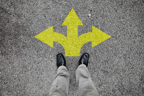 یک جفت پا ایستاده روی یک جاده آسفالته با چاپ فلش زرد که به سه جهت مختلف برای مفهوم تصمیم گیری در چهارراه اشاره می کند