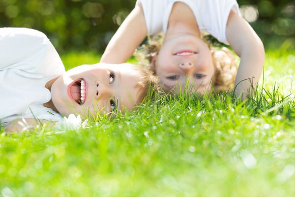 کودکان شادی که وارونه روی چمن های سبز ایستاده اند دختر و پسر در پارک بهار مفهوم سبک زندگی سالم