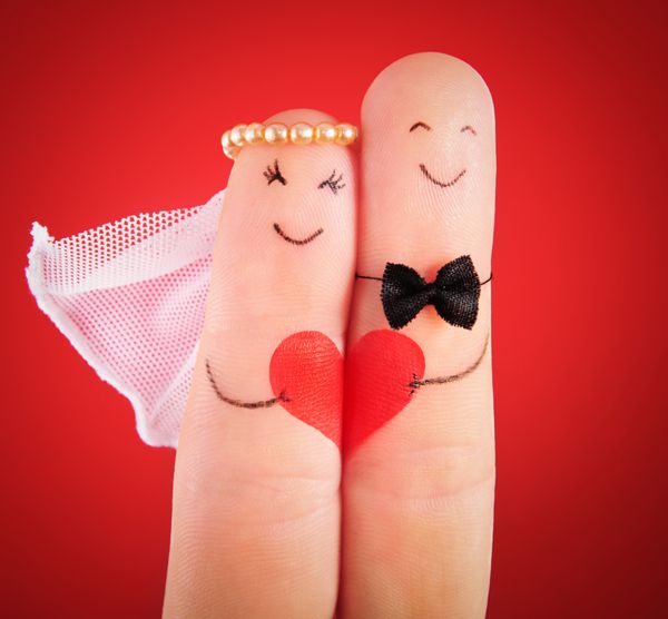 مفهوم عروسی - تازه ازدواج کرده ها با انگشتان خود در برابر پس زمینه قرمز نقاشی شده اند