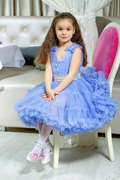 دختر کوچک فرفری با لباس آبی روی صندلی نشسته است