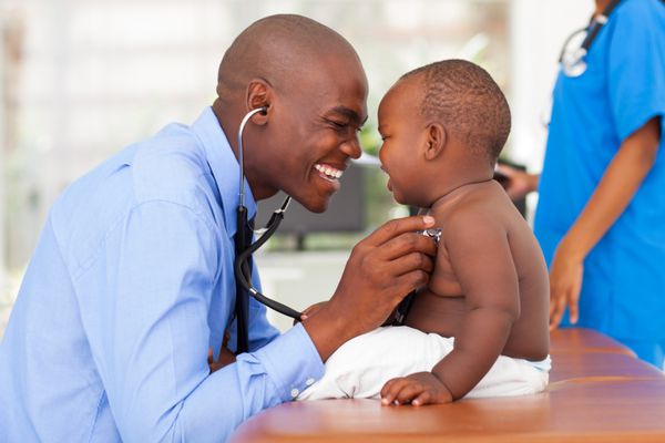 دکتر مرد آفریقایی خوشحال در حال معاینه نوزاد پسر با پرستار زن در پس زمینه