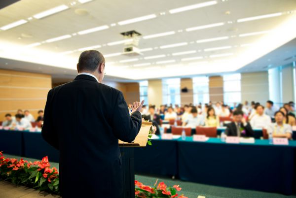 مرد بازرگان در حال سخنرانی در مقابل یک مخاطب بزرگ در یک سالن کنفرانس است