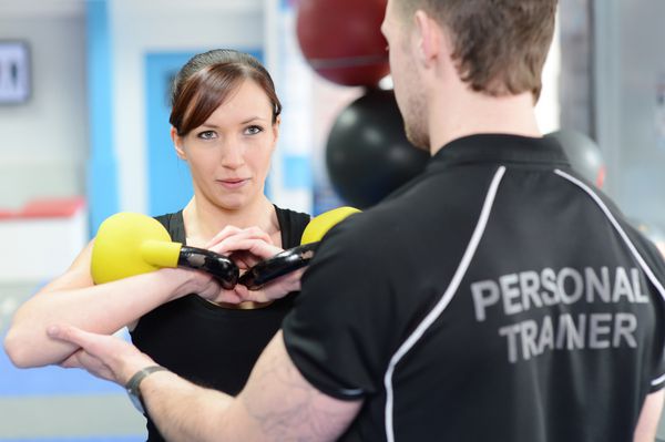 زن جوان با وزنه های زنگ کتری با مربی شخصی در باشگاه ورزش می کند