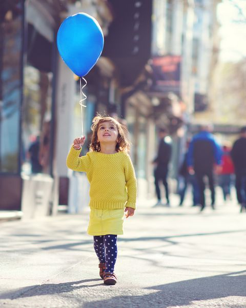 دختر بچه ای که با بادکنک آبی در خیابان راه می رود