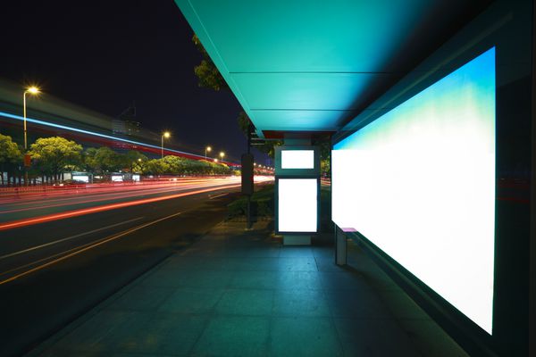 مسیرهای نور اتومبیل های جاده ای در جعبه های نور تبلیغاتی شهری مدرن می گذرد