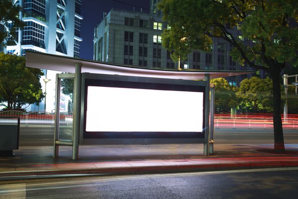 مسیرهای نور اتومبیل های جاده ای در جعبه های نور تبلیغاتی شهری مدرن می گذرد