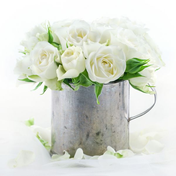 دسته گل رز سفید عروسی در یک فنجان فلزی قدیمی در پس زمینه l رویایی با گلبرگ های گل
