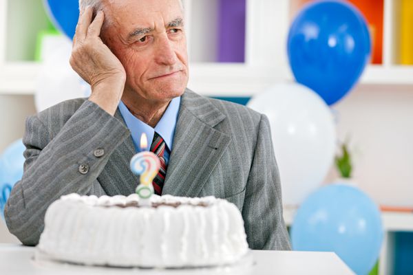 مرد سالخورده ای جلوی کیک تولد نشسته و سعی می کند چند سالش را به خاطر بیاورد