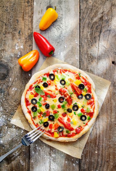 نمای بالای یک پیتزای خوشمزه و رنگارنگ خانگی با پوسته طلایی ضخیم و روی آن پنیر فلفل گوجه فرنگی و زیتون