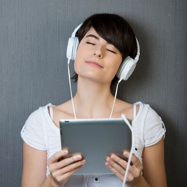 زن جوان در حال لذت بردن از موسیقی خود با گوش دادن به مجموعه ای از گوشی های متصل به رایانه لوحی خود