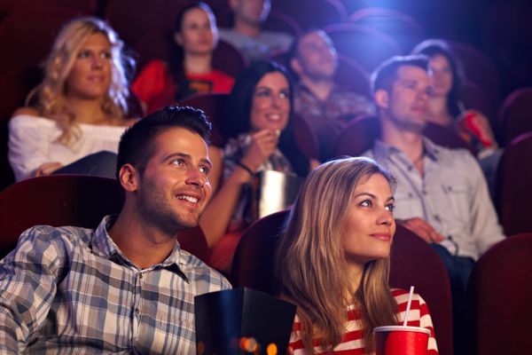 جوانانی که در سالن سینما نشسته اند و فیلم تماشا می کنند