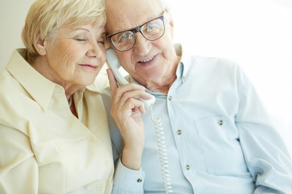 پرتره مرد سالخورده ای که در حالی که با همسرش در نزدیکی تلفن صحبت می کند به دوربین نگاه می کند