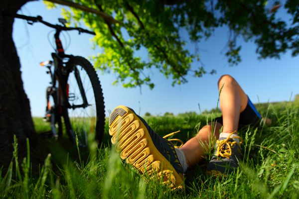 خانم جوانی که بعد از دوچرخه سواری روی یک چمنزار سبز استراحت می کند روی یک پا تمرکز کنید