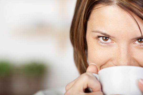 پرتره نزدیک از یک زن زیبا که لبخند می‌زند و قهوه می‌نوشد