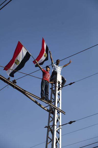 قاهره مصر - 1 ژوئیه دو جوان مصری در تظاهرات 30 ژوئن علیه محمد مرسی در حالی که پرچم مصر را در نزدیکی رفیق الاتهادیا در دست داشتند در بالای تیر تراموا تظاهرات کردند قاهره - 1 ژوئیه 2013
