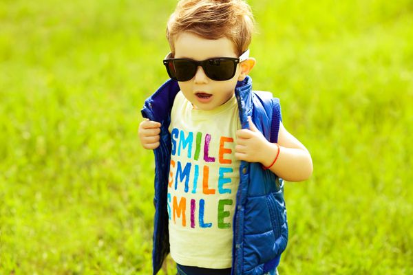 نوزاد پسر شیک با موهای زنجبیلی قرمز با عینک آفتابی مد روز و ژاکت آبی ایستاده در پارک سبک هیپستر هوای آفتابی کلمه لبخند چاپ شده روی تی شرت copy-sp بیرون از خانه