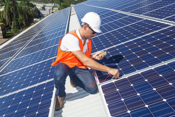 تکنسین جوان در حال بررسی پنل های خورشیدی روی سقف کارخانه
