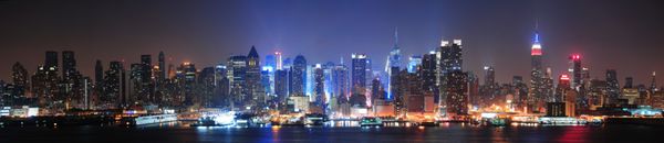 خط افق مرکز شهر نیویورک منهتن در شب با آسمان‌خراش‌هایی که بر فراز رودخانه هادسون با انعکاس روشن شده‌اند