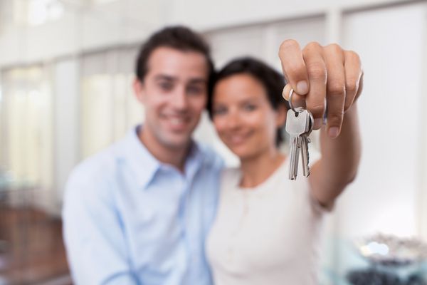 زوج جوان شاد و خندان در حال نشان دادن کلیدهای خانه جدیدشان
