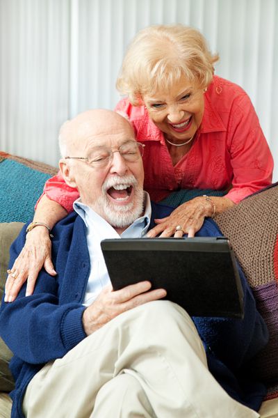زوج سالخورده ای که در حال استفاده از رایانه لوحی خود هستند که سرگرم سرگرمی و خندیدن هستند