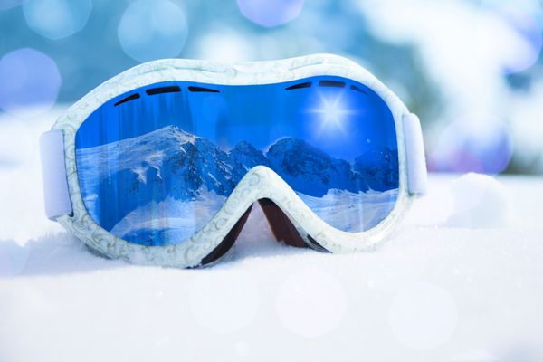 نمای نزدیک از ماسک اسکی و اسنوبرد با انعکاس کوه در آن