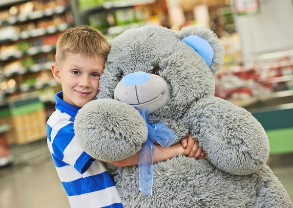 پسر بچه کوچک با هدیه خرس مخمل خواب دار بزرگ در اسباب بازی فروشی یا فروشگاه سوپرمارکت