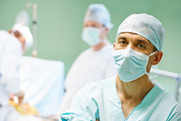 پرتره پزشک جراح در مقابل جراحان در حال انجام عمل بر روی یک بیمار در کلینیک جراحی قلب