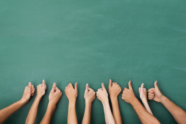 نمای نزدیک از دستان گروهی از افراد که در حالی که دستانشان را روی تخته سیاه سبز خالی با کپی اسپرت بلند کرده اند با اشاره به نشانه تایید موفقیت نشان می دهند