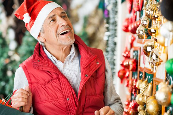 مرد مسن خوشحال در حال انتخاب زیور آلات کریسمس در فروشگاه