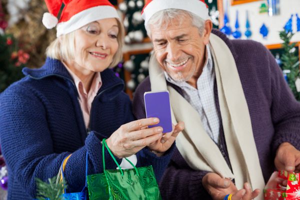 زوج سالمند شادی که با هم در فروشگاه کریسمس از تلفن همراه استفاده می کنند