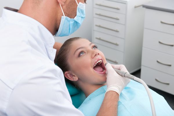 بیمار کوچک در مطب دندانپزشکی نمای بالای دختر نوجوانی که روی صندلی مطب دندانپزشکی نشسته در حالی که دکتر در حال معاینه دندان است